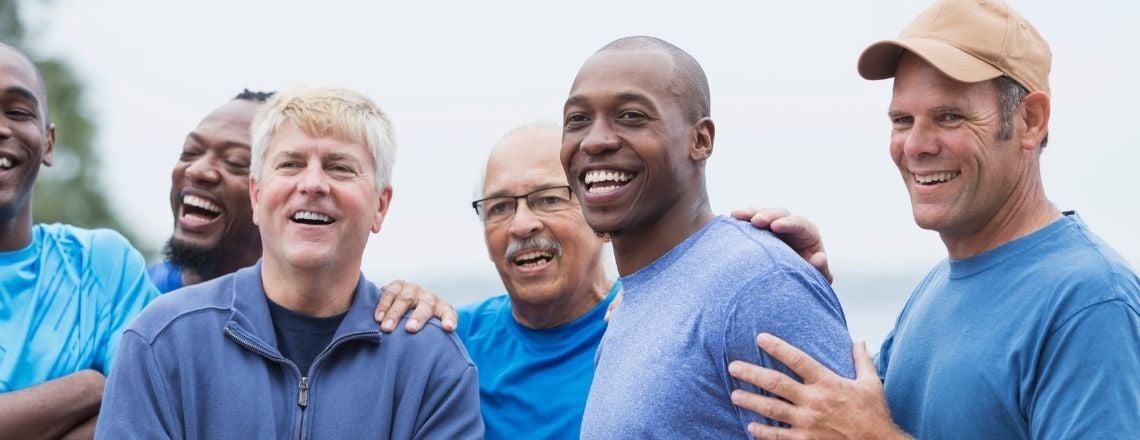 A diverse group of smiling men of various ages standing together outdoors.