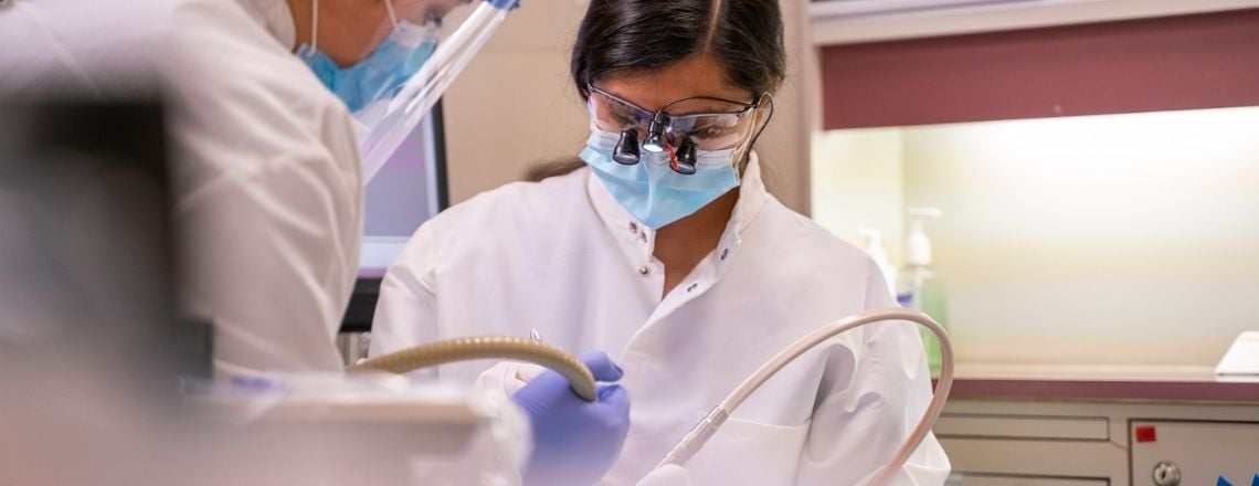 A female dentist wearing protective loupes and a face mask performing a clinical dental procedure.
