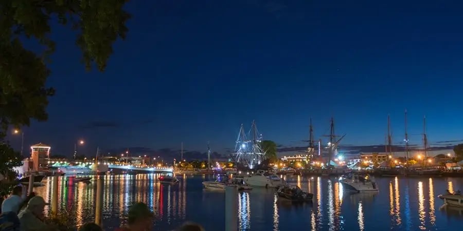 Illuminated tall ships and boats docked along the Green Bay waterfront at night.