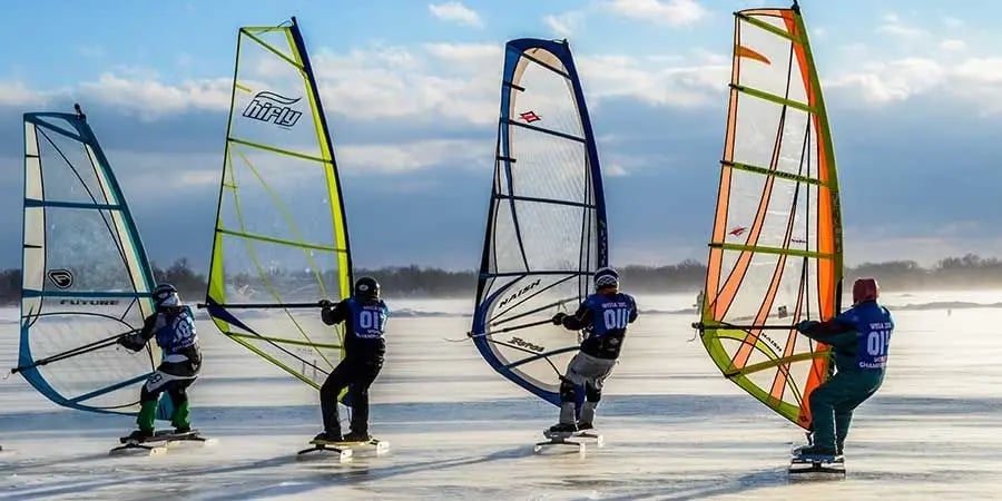 Four ice windsurfers with colorful sails lined up on frozen Lake Winnebago in Fond du Lac, Wisconsin.