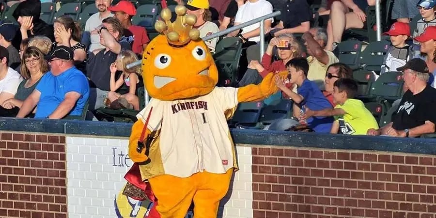 The Kenosha Kingfish baseball mascot high-fives a young fan in the stadium stands.