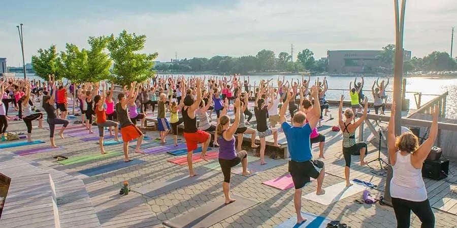 A large group of people practicing tree pose during an outdoor yoga class on a boardwalk in Green Bay, Wisconsin.