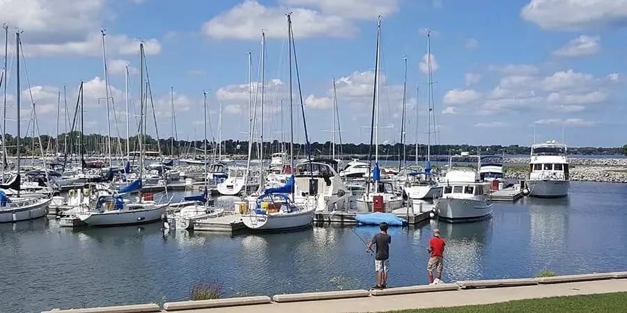 Two boys fishing at a sunny marina filled with docked sailboats in Racine, Wisconsin.