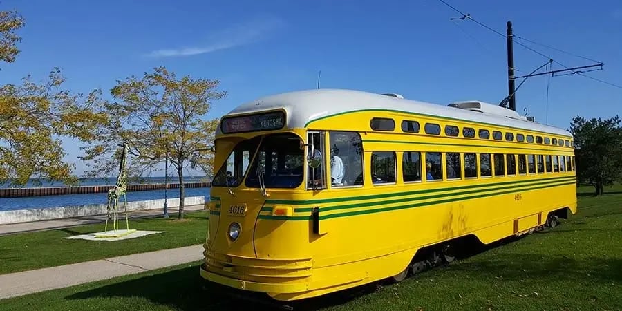 A vintage yellow Kenosha streetcar on a grassy track near the lakefront.