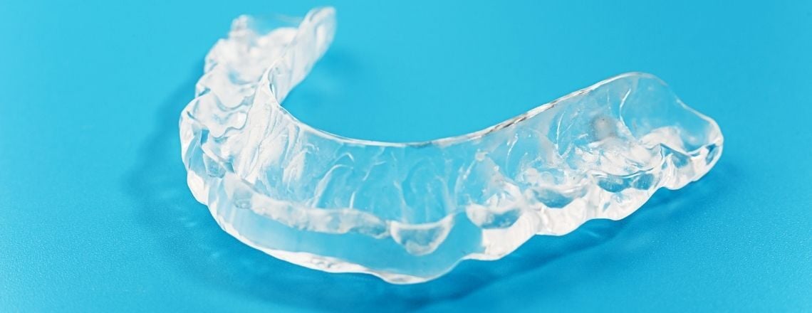 Clear plastic dental aligner sitting on a bright blue background.