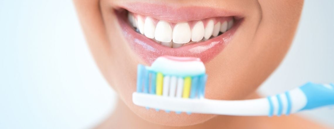 young woman smiling while holding a toothbrush with toothpaste on it