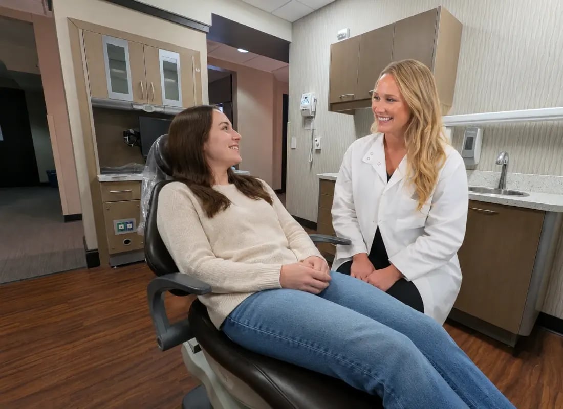 A female dentist smiling and consulting with a patient sitting in a dental chair.