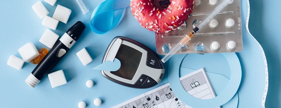 Blood glucose meter, insulin syringe, pills, sugar cubes, and a pink donut representing diabetes management.