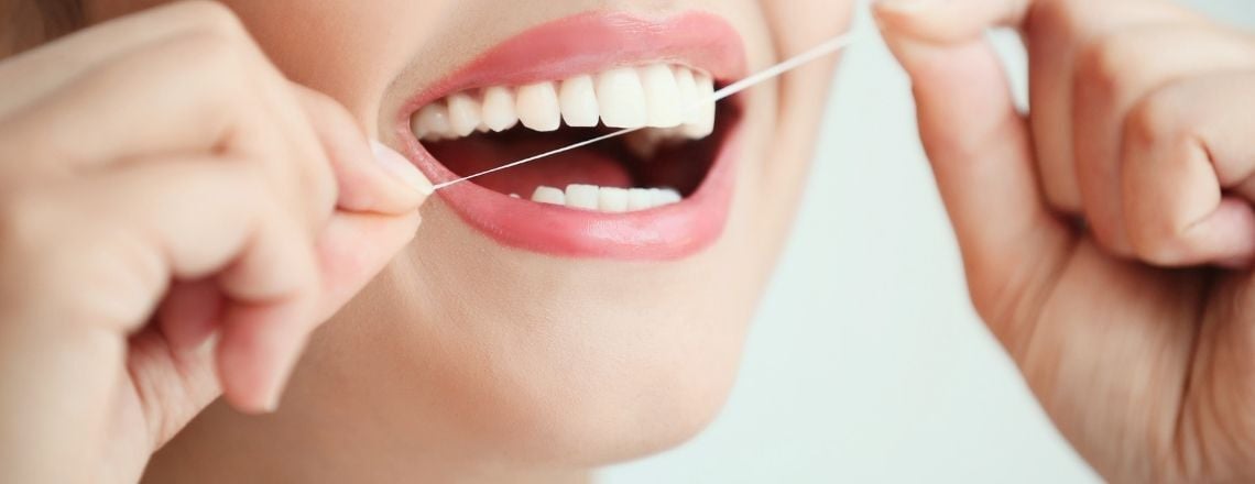 young woman smiling and flossing her teeth