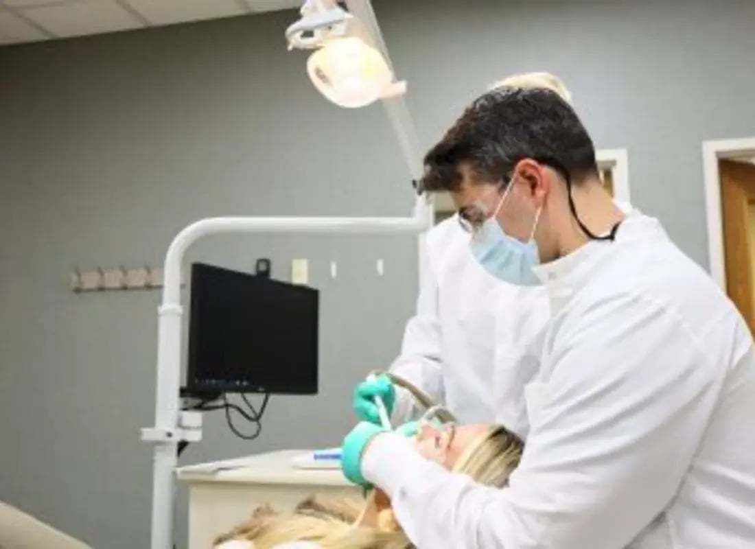 A dentist and assistant perform a dental procedure on a patient in a clinic.