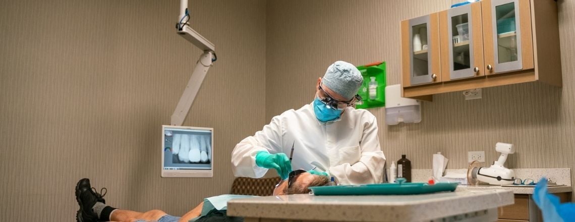 A dentist wearing protective gear performs a dental procedure on a patient.