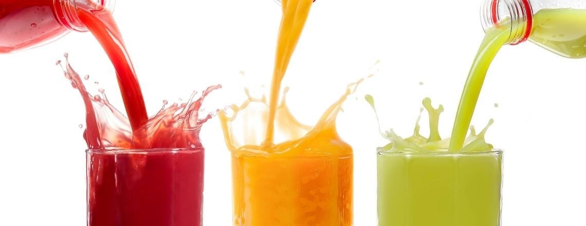 Red, orange, and green fruit juices splashing as they are poured into glasses against a white background.