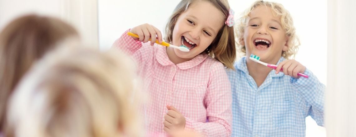 two children smiling in the mirror while brushing their teeth