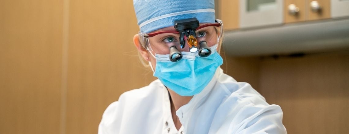 dentist working on a patient with loupes and protective mask and hat on