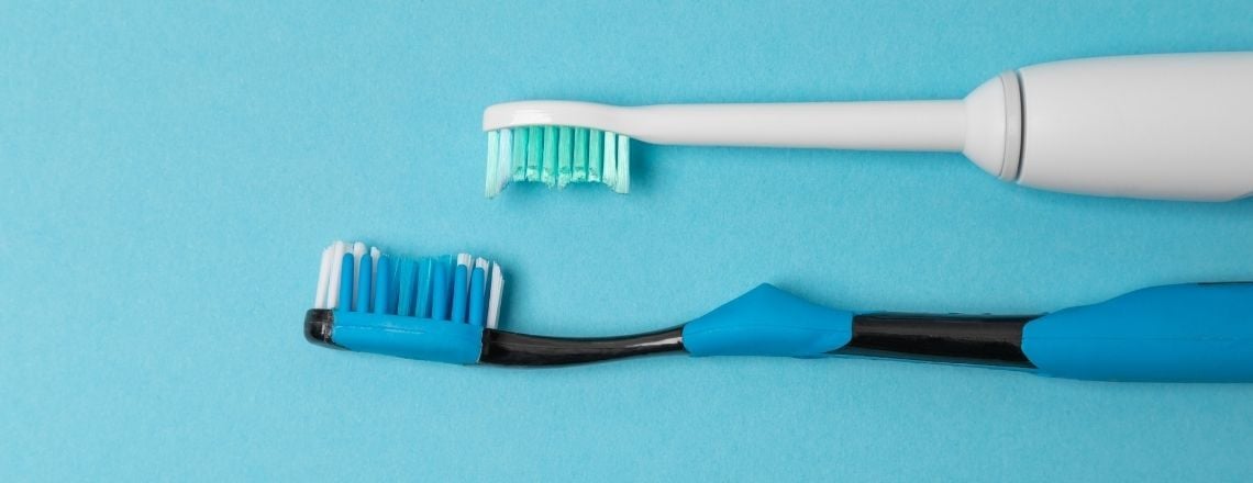 An electric toothbrush and a manual toothbrush laid flat on a solid blue background.