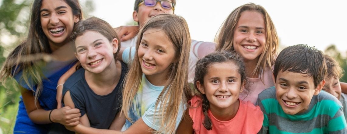 A diverse group of happy, smiling children posing together outdoors.