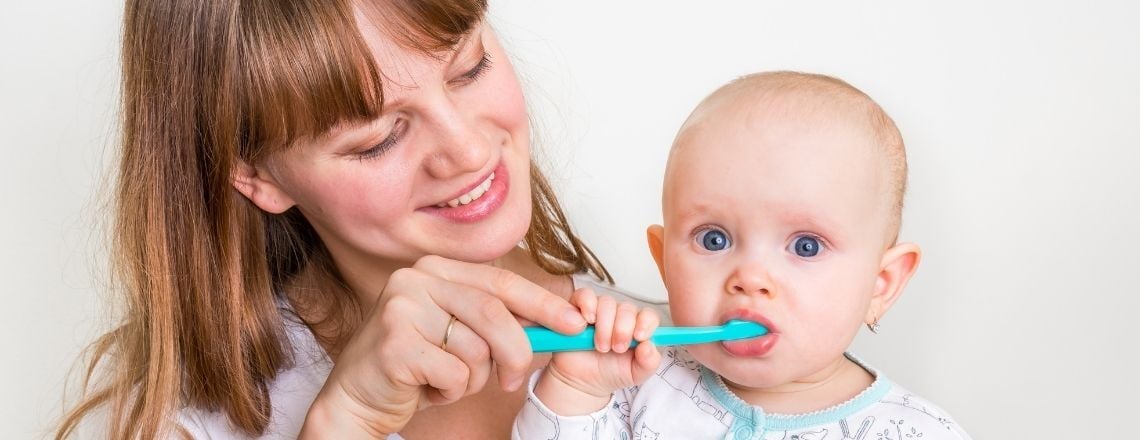 Mother brushing her baby's teeth with a toothbrush while smiling