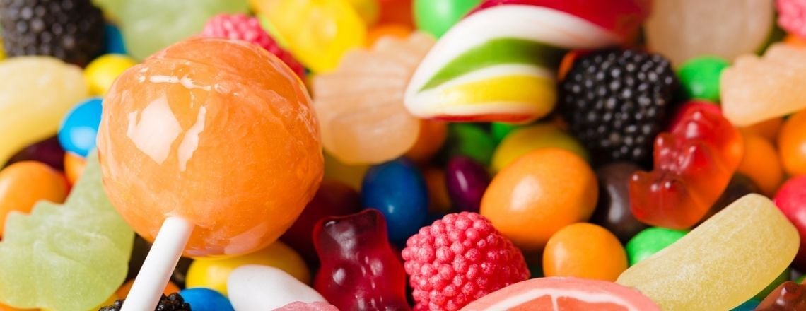 A colorful close-up assortment of candies featuring an orange lollipop, gummy bears, and jelly beans.
