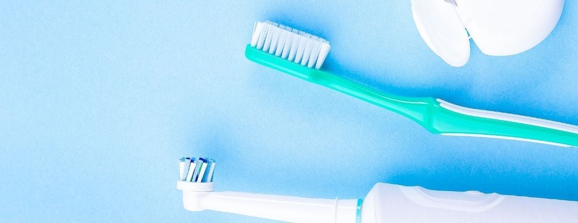 Manual and electric toothbrushes displayed next to dental floss on a light blue background.