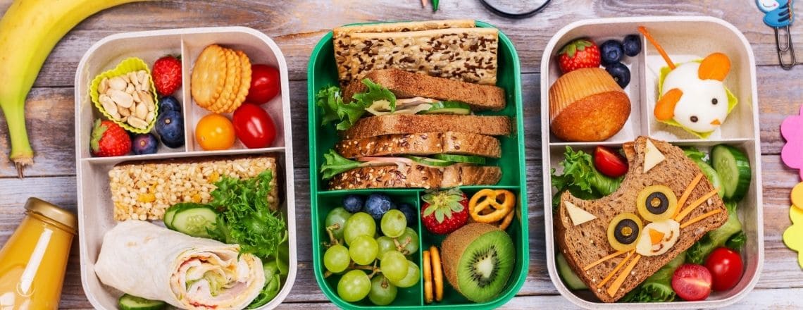 Three creative school lunch boxes filled with healthy sandwiches, wraps, fruits, and veggies.