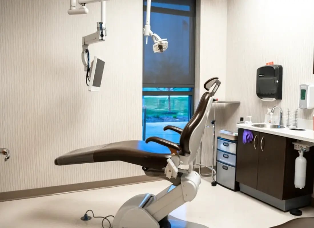A modern brown leather dental chair in a clean, fully equipped clinical treatment room.