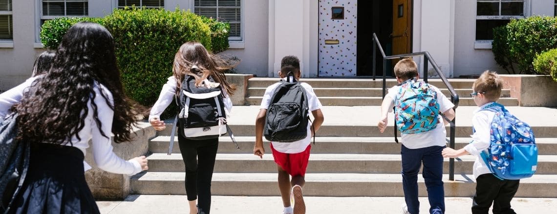 Diverse group of elementary school children running up steps into a school building.