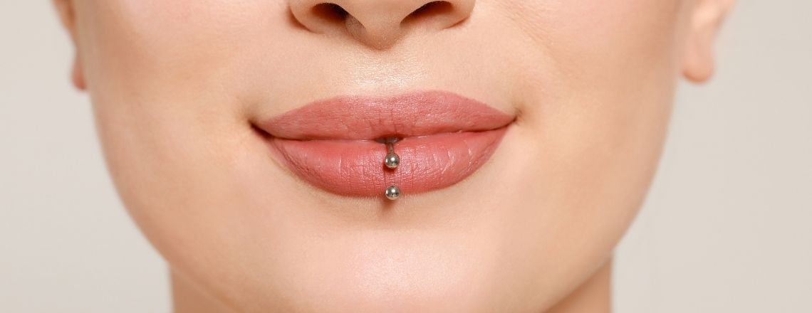 Close-up of a vertical labret piercing with silver barbell beads on a person's bottom lip.