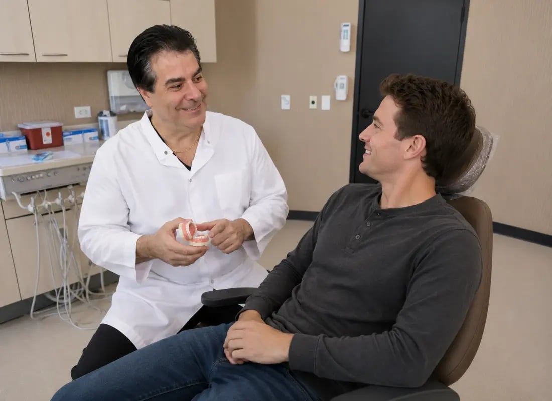 An oral surgeon uses a teeth model to explain a procedure to a patient in a dental chair.