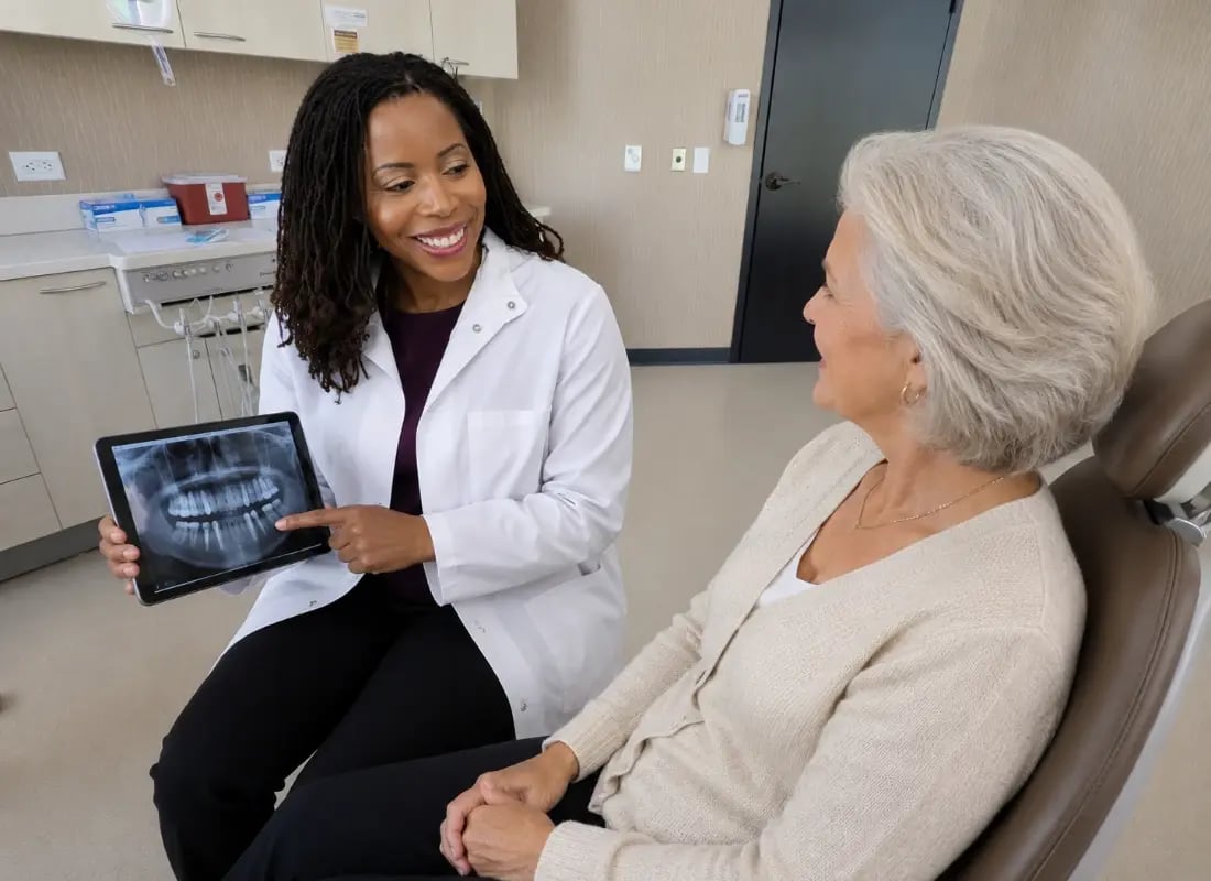 A prosthodontist shows a dental X-ray on a tablet to a senior patient during a consultation.