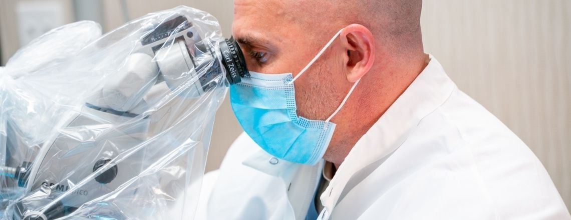 A dentist wearing a protective mask uses a Carl Zeiss dental microscope for precision treatment.