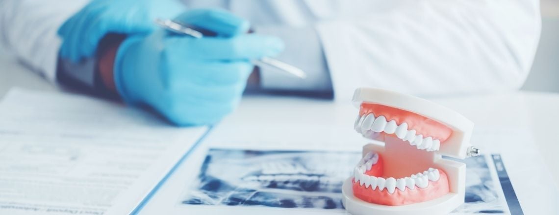 model of teeth on a table with an x-ray image and a dentist reviewing the x-ray