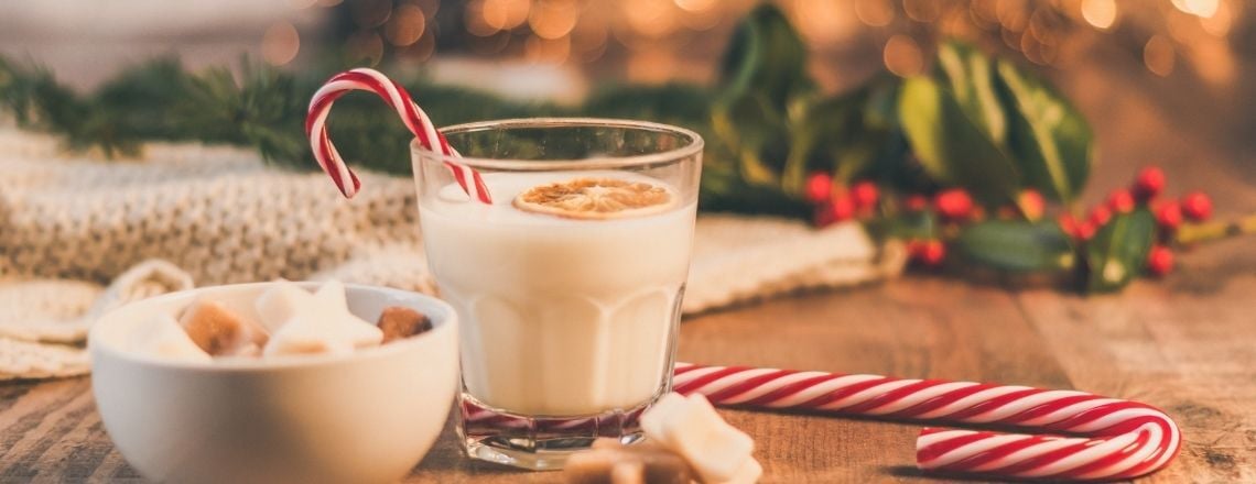 cup of eggnog with candy canes and holly surrounding it