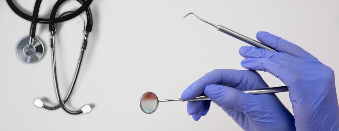 Hands in blue gloves holding dental instruments next to a medical stethoscope.