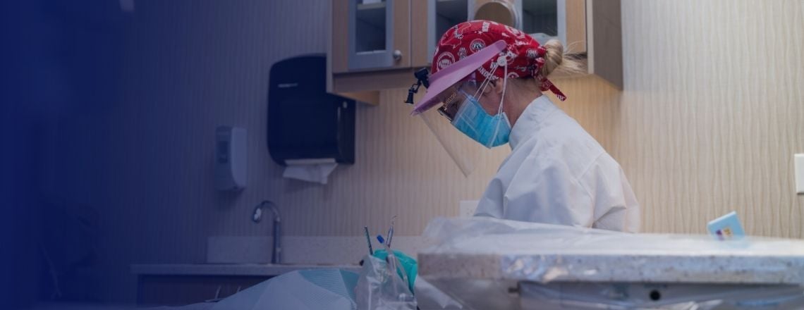 Dental hygienist wearing protective face shield and mask performing a dental procedure.