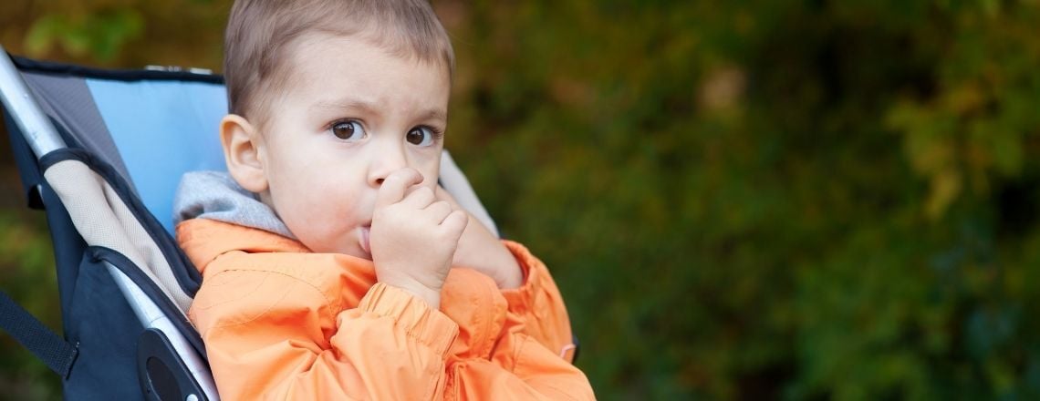 young child sitting in a stroller sucking his thumb