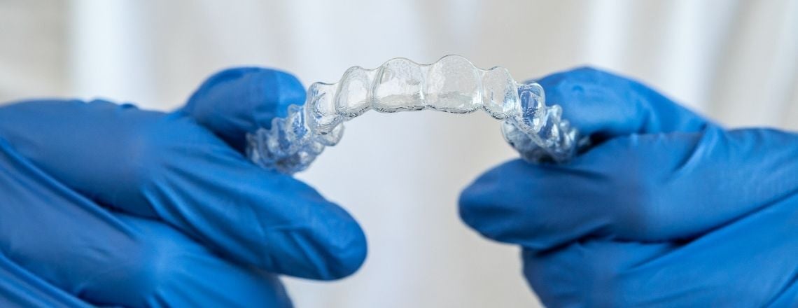 person wearing blue gloves holding a clear retainer