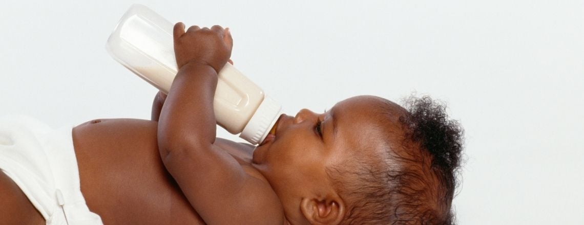 young baby laying down drinking milk out of a baby bottle