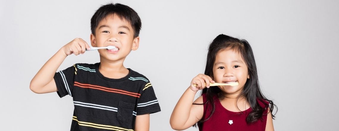 two young children brushing their teeth with regular toothpaste and toothbrushes
