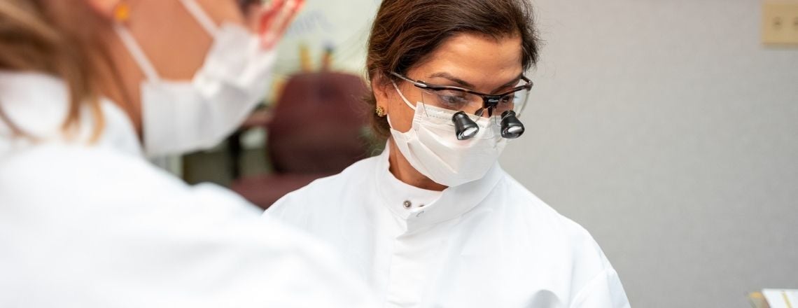 female dentist with loupes glasses talking to a patient in a dental chair 