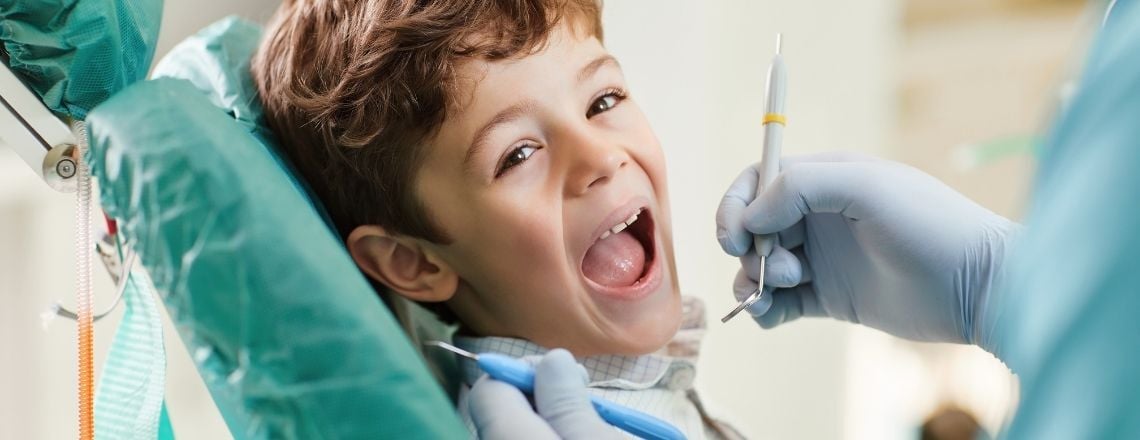 young child in a dental chair smiling with his mouth open 