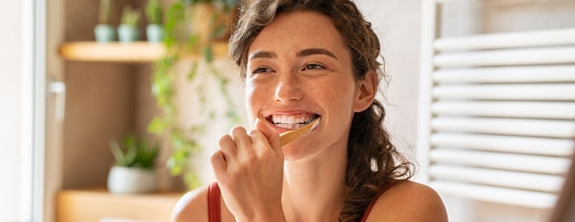 young woman brushing her teeth and smiling into the mirror