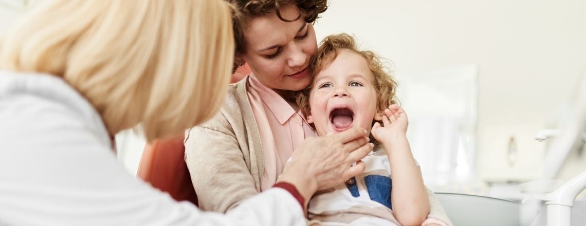 woman holding her child and a female dentist examining the child's mouth