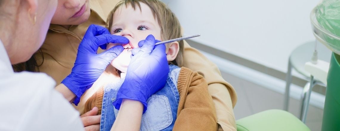 young child sitting on a a parent's lap being examined by a dentist