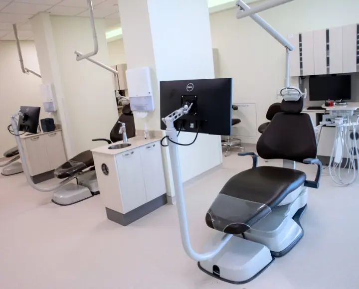 A row of modern dental chairs equipped with monitors in a bright clinic setting.