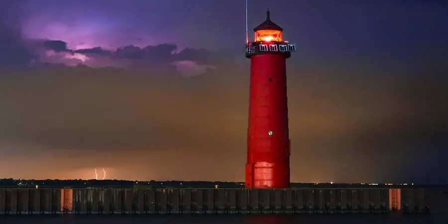 The red Kenosha North Pier Lighthouse illuminated during a purple lightning storm at night.