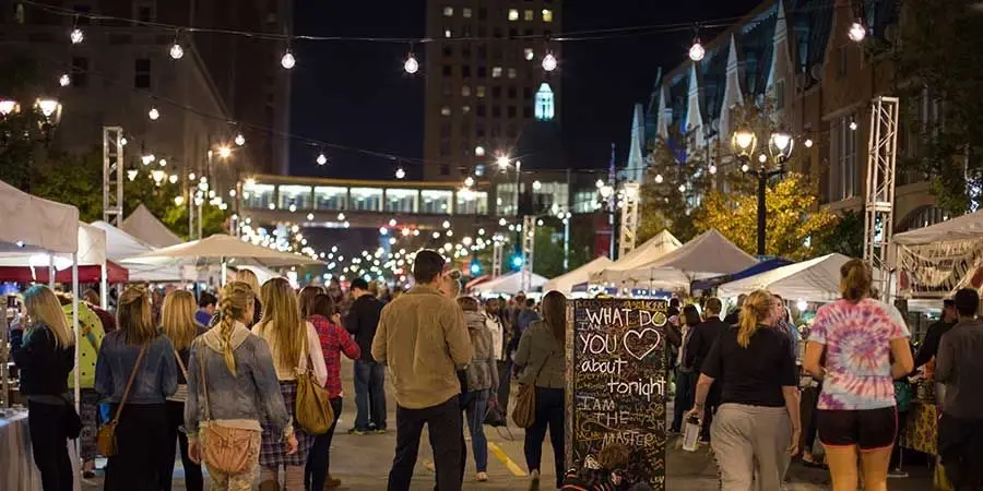 People stroll through a lively outdoor night market in Milwaukee, Wisconsin, under glowing string lights.