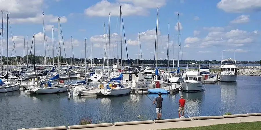 Two boys fishing at a sunny marina filled with docked sailboats in Racine, Wisconsin.