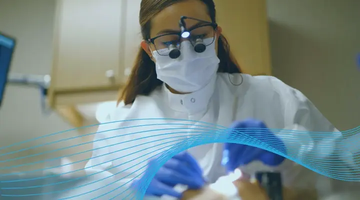 Female dental hygienist wearing magnifying loupes performs a dental procedure on a patient.