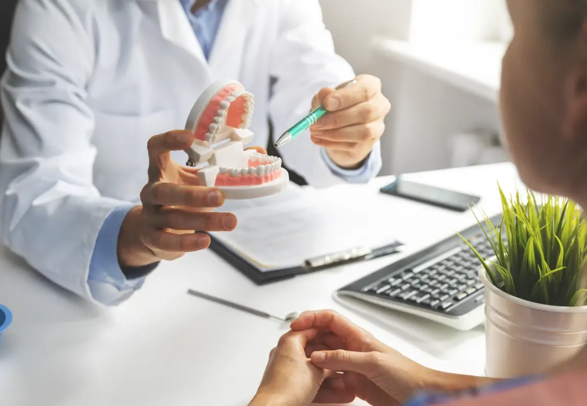 A dentist uses a plastic teeth model to explain a dental treatment to a patient during a consultation